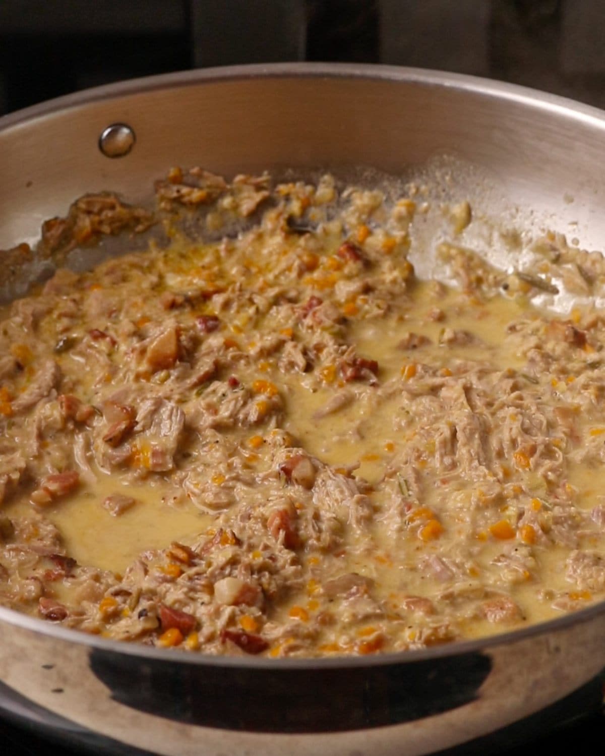 Pork ragu simmering in a stainless steel fry pan.