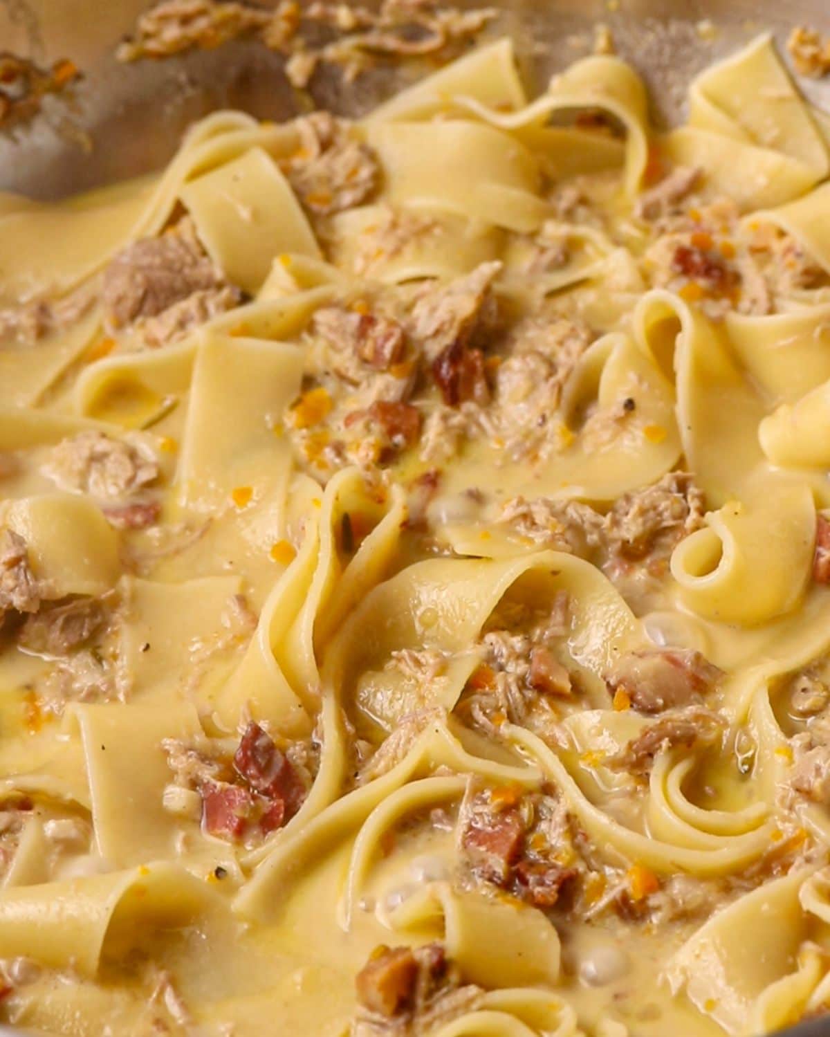 Cooked pappardelle pasta bubbling with the sauce in the pan.