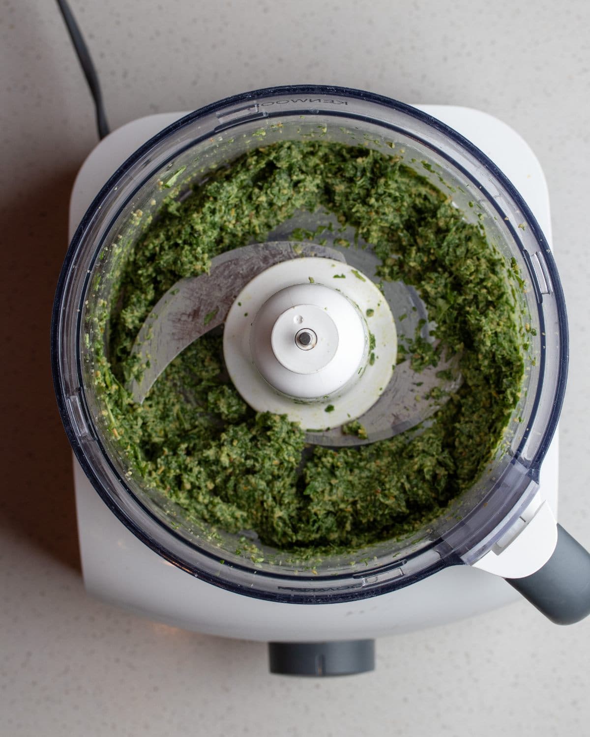Food processor with blended pesto inside.