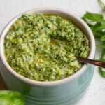 A ramekin of arugula pesto with a teaspoon resting in.