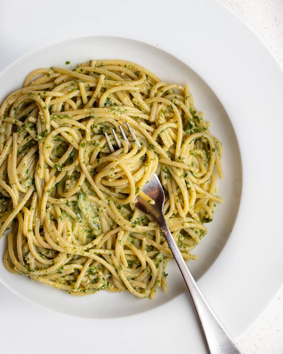 Finished pesto spaghetti on a white plate with a fork resting in.