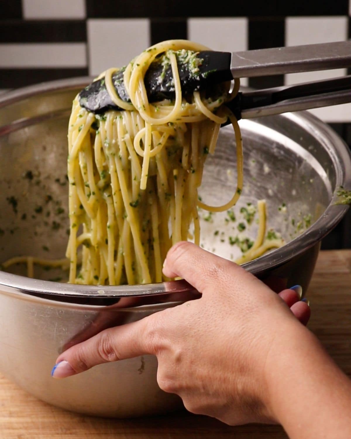 Tongs holding up spaghetti coated in a pesto sauce.