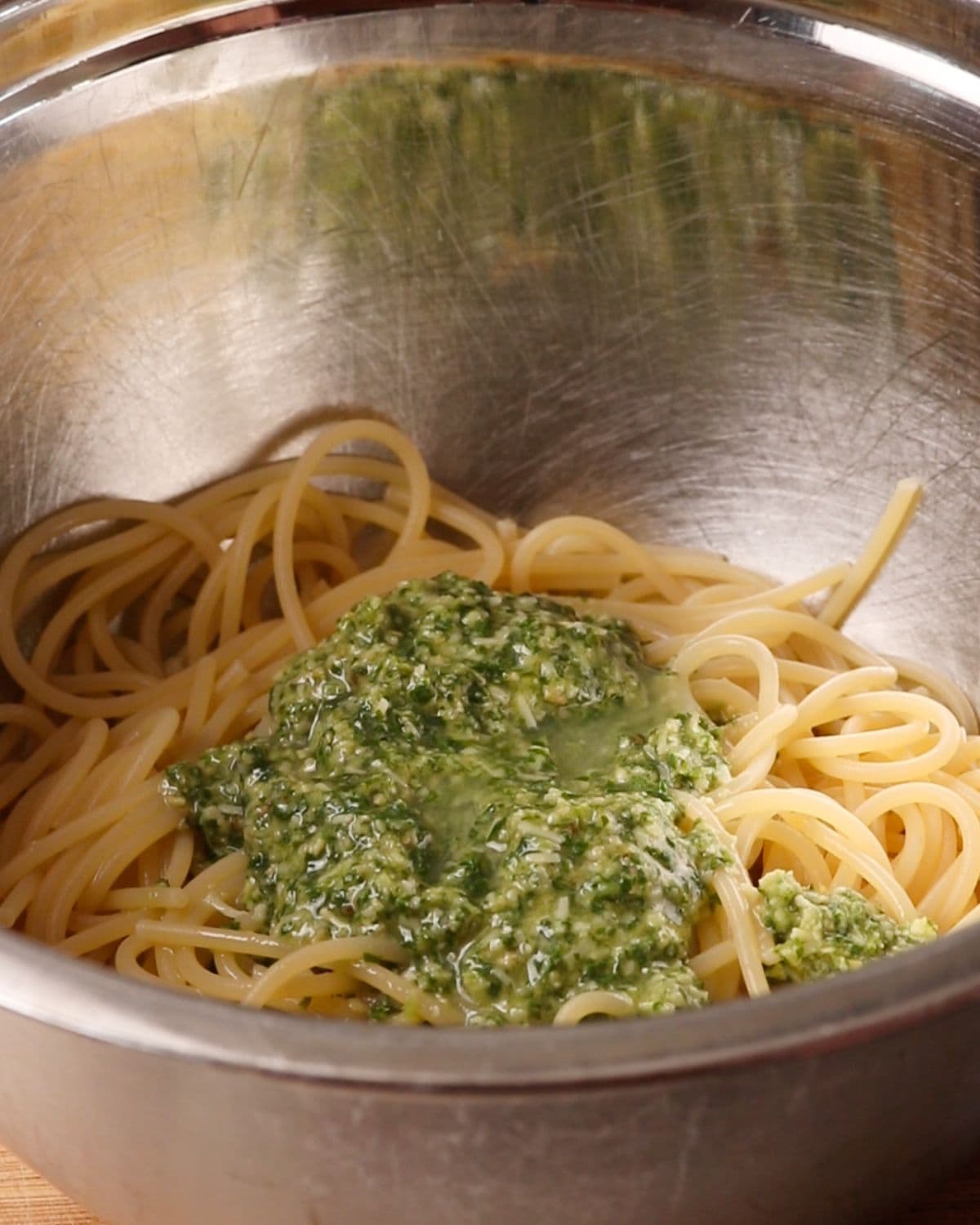 Mixing bowl with cooked spaghetti and pesto on top.