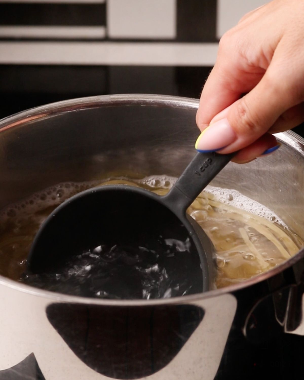 A measuring cup being dipped into pasta water.