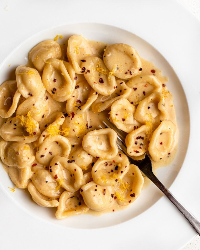 White plate with cooked orecchiette pasta in a creamy roast garlic and lemon sauce. Fork resting to the right.