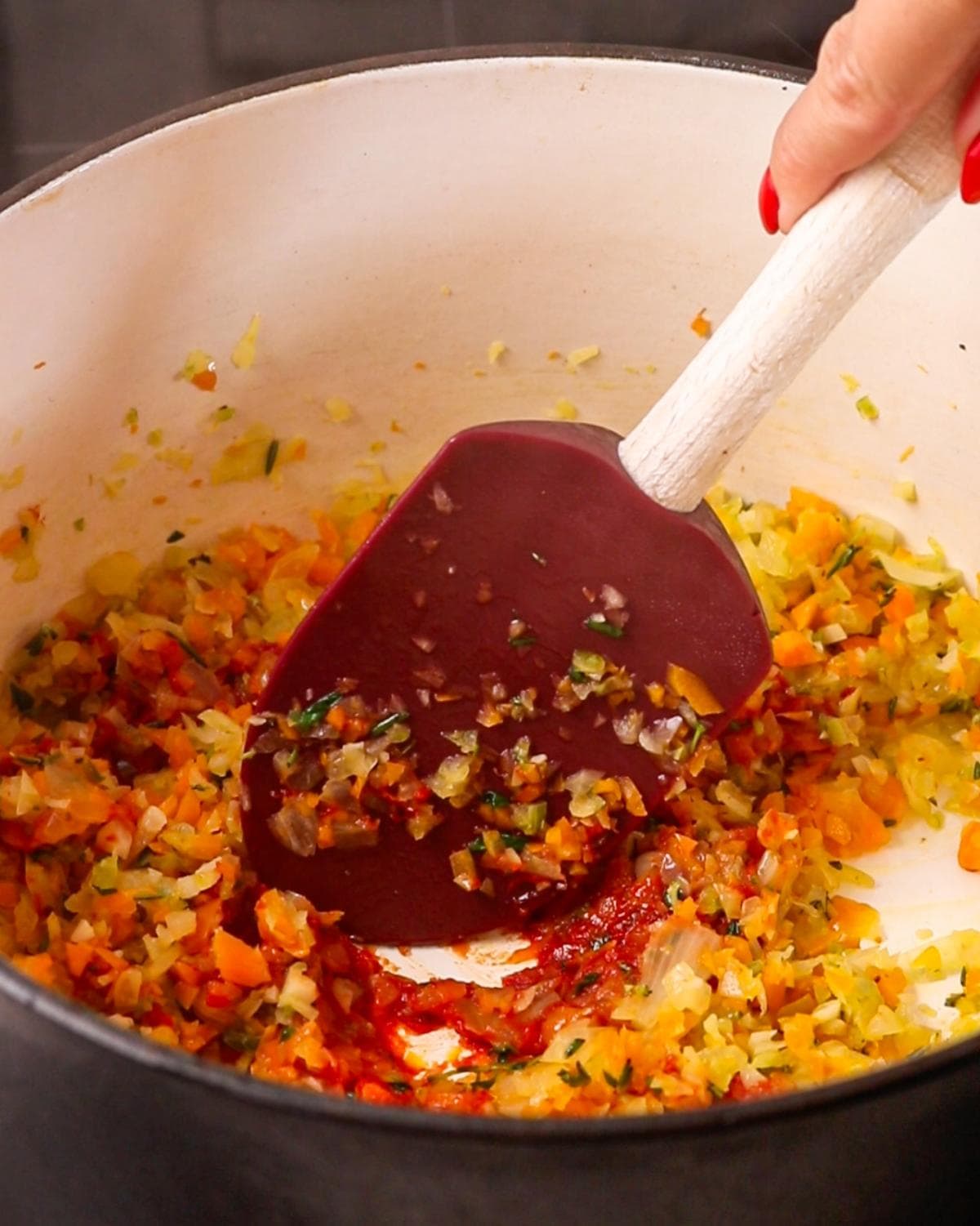 Soffritto with tomato paste, garlic and herbs cooking in a Dutch oven.