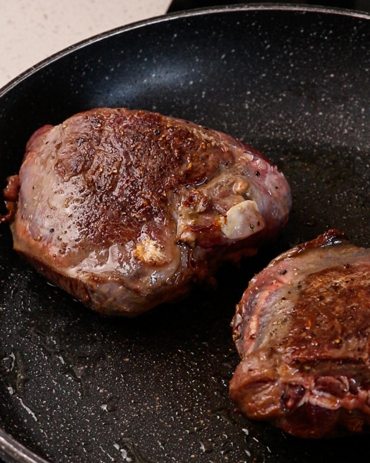 Beef cheeks browning in a frying pan before making beef cheek ragu.