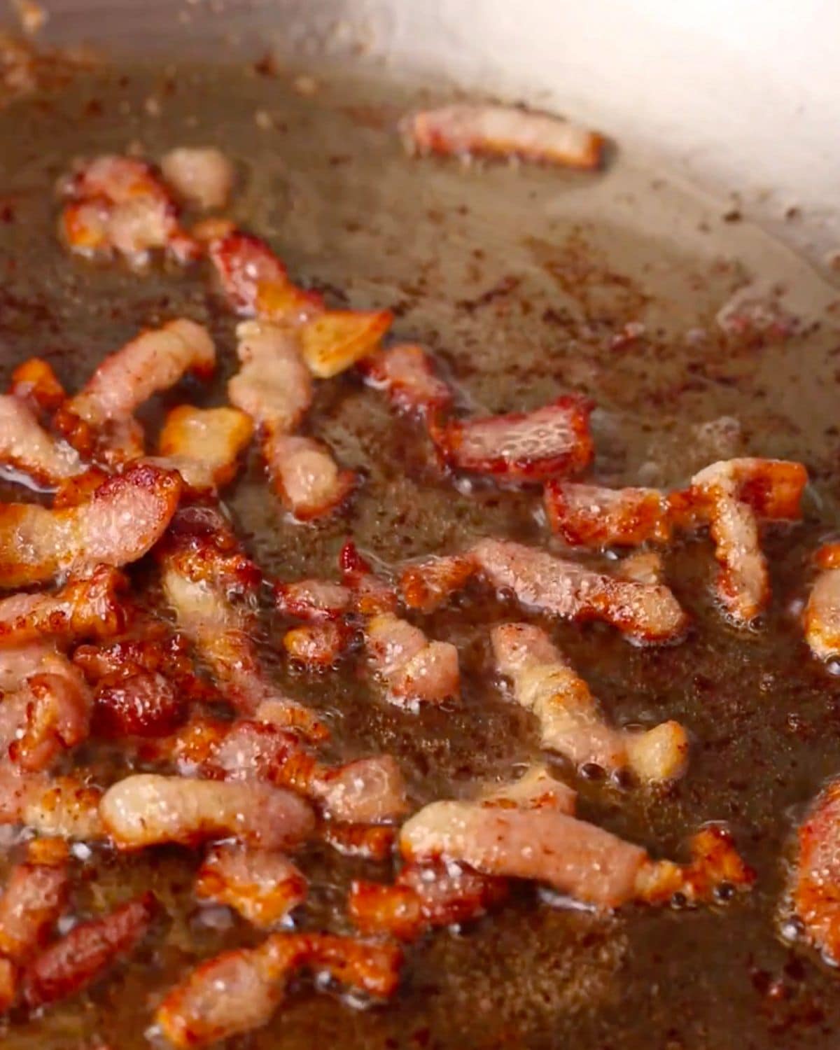 Bacon pieces sizzling in a skillet.