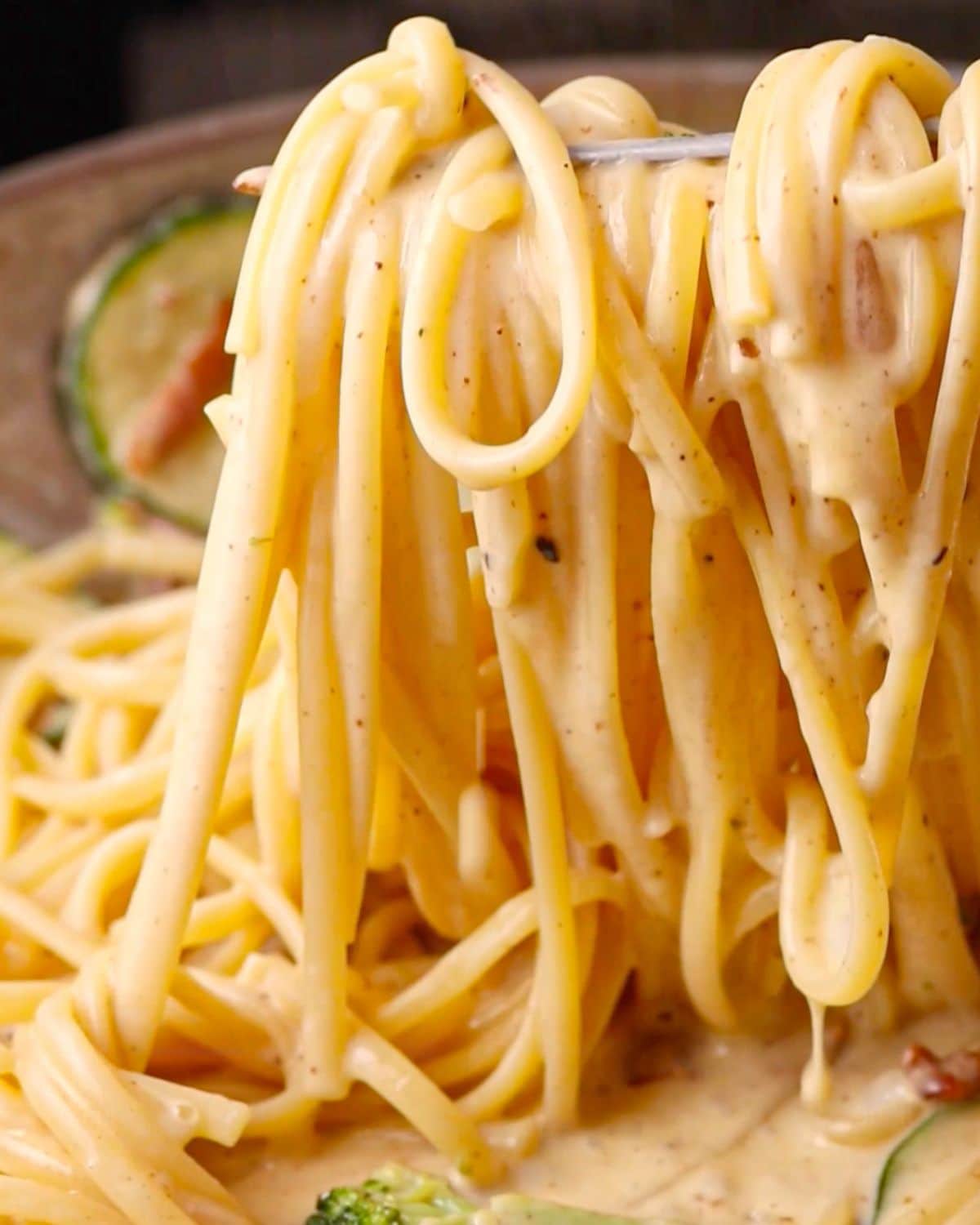 Tongs holding up the cooked pasta with creamy sauce dripping.