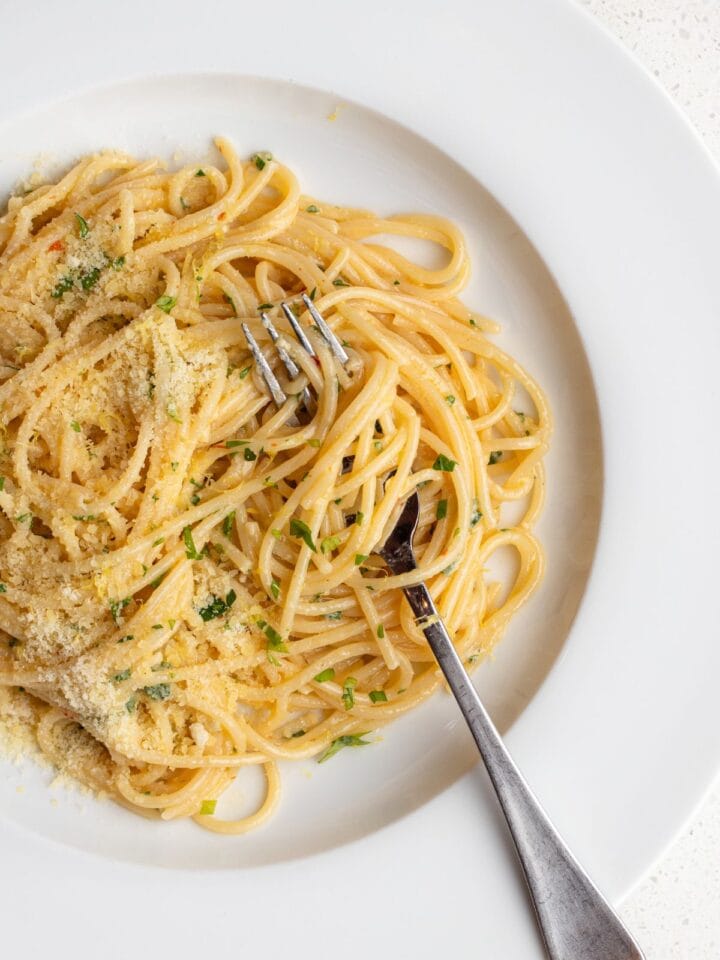 White plate with spaghetti in a lemon butter sauce. Fork resting in.