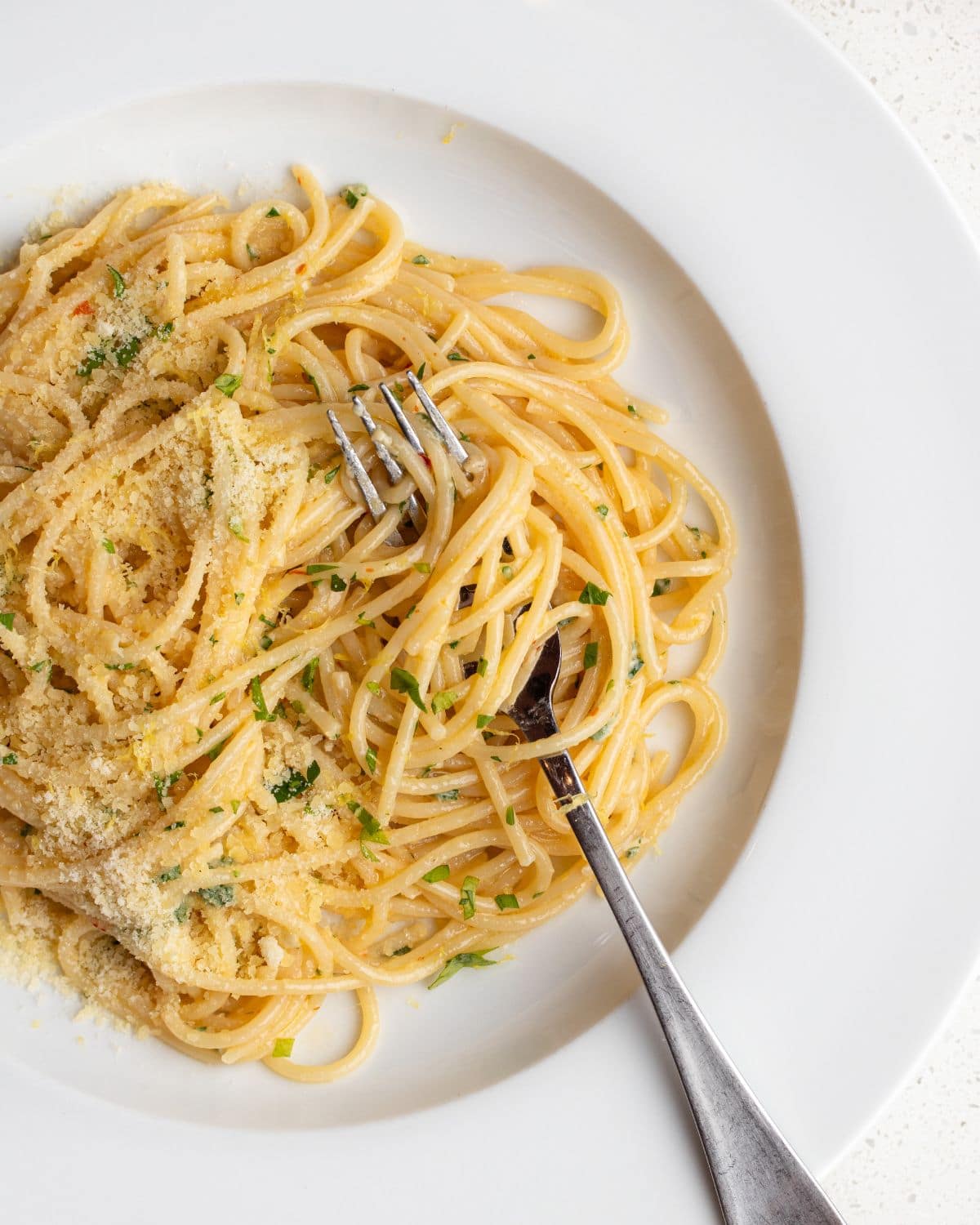 White plate with spaghetti in a lemon butter sauce. Fork resting in.