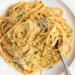 White plate with spaghetti in a lemon butter sauce. Fork resting in.