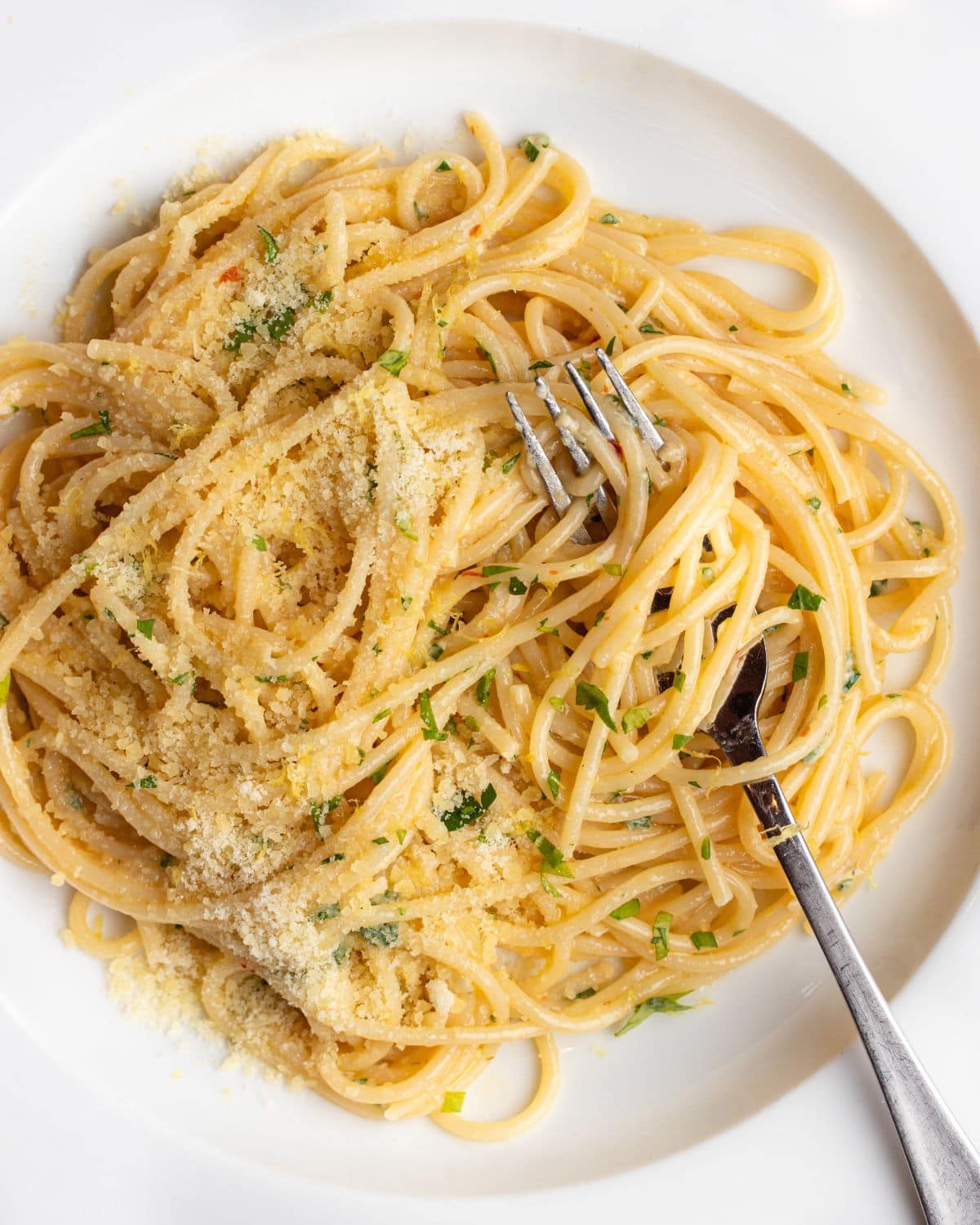 White plate with spaghetti in a lemon butter sauce. Fork resting in.