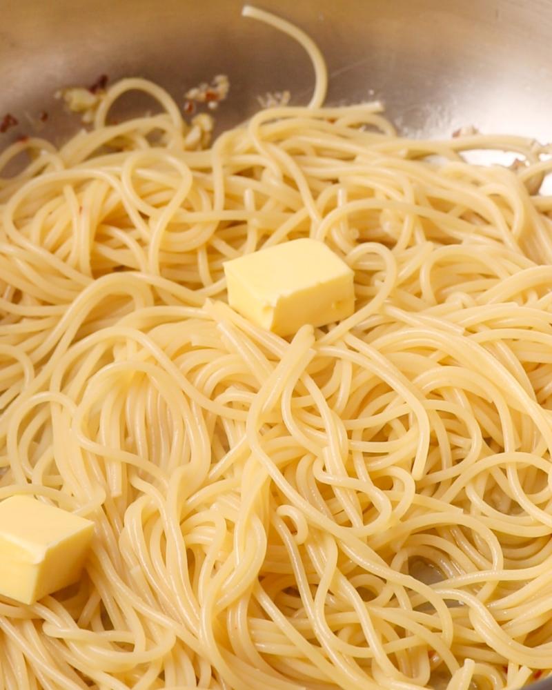 Spaghetti in the pan with cubes of butter on the top.