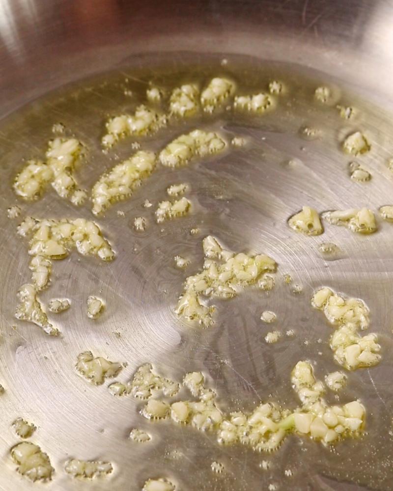 Garlic sizzling in olive oil in a stainless steel pan.
