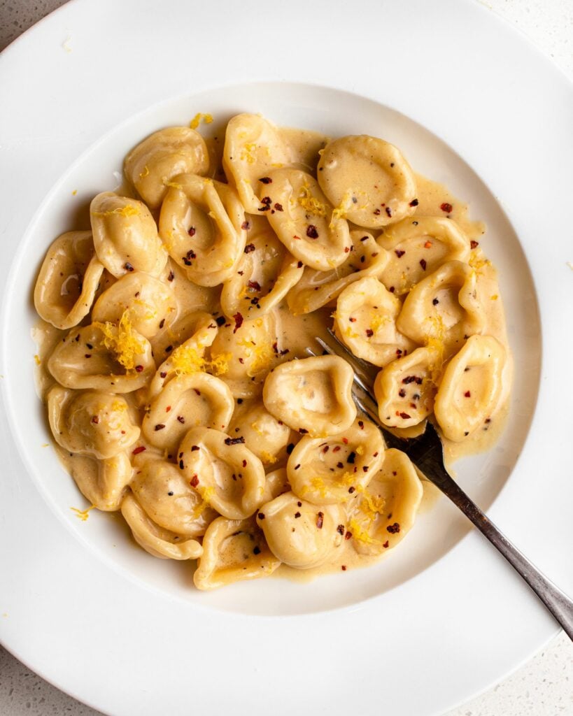 Cooked orecchiette pasta in a creamy roast garlic and lemon pasta sauce on a white plate. Fork is resting into the pasta on bottom right.