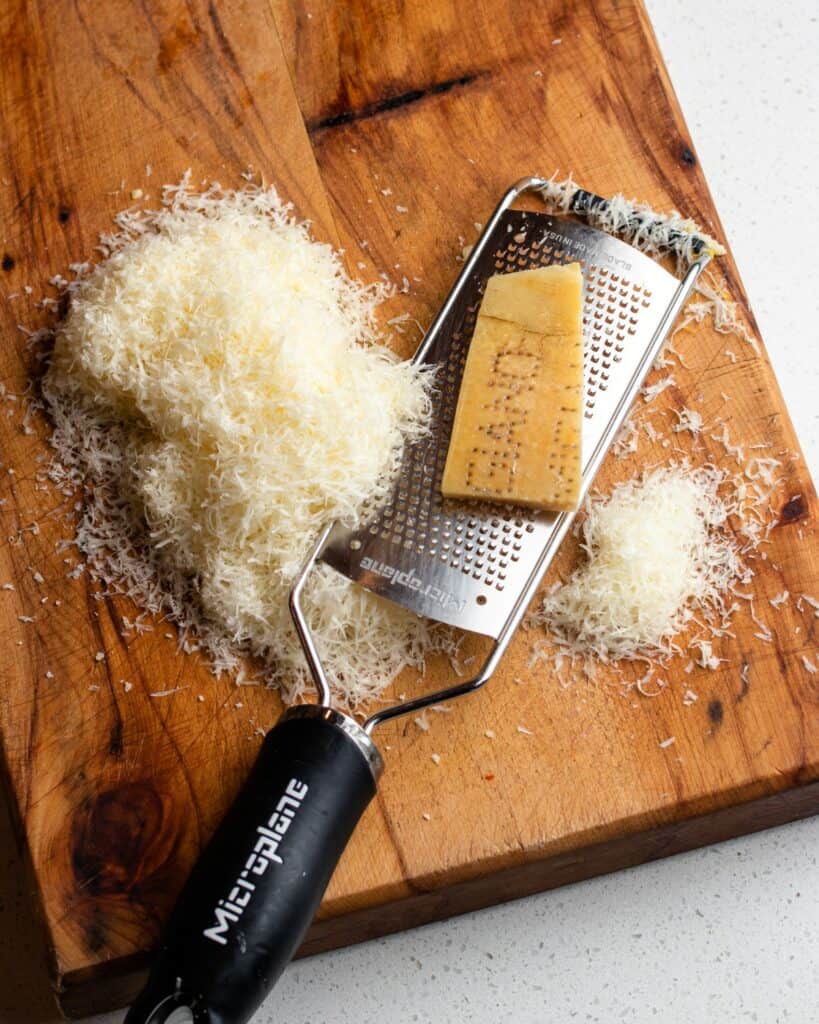 Grated parmesan with a microplane grater on top on a wooden chopping board.