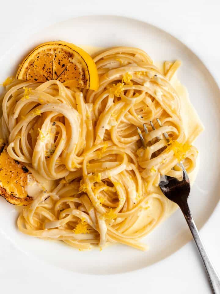 Linguine in a creamy lemon sauce. Charred lemon slices to left and a fork twirling into noodles at right.