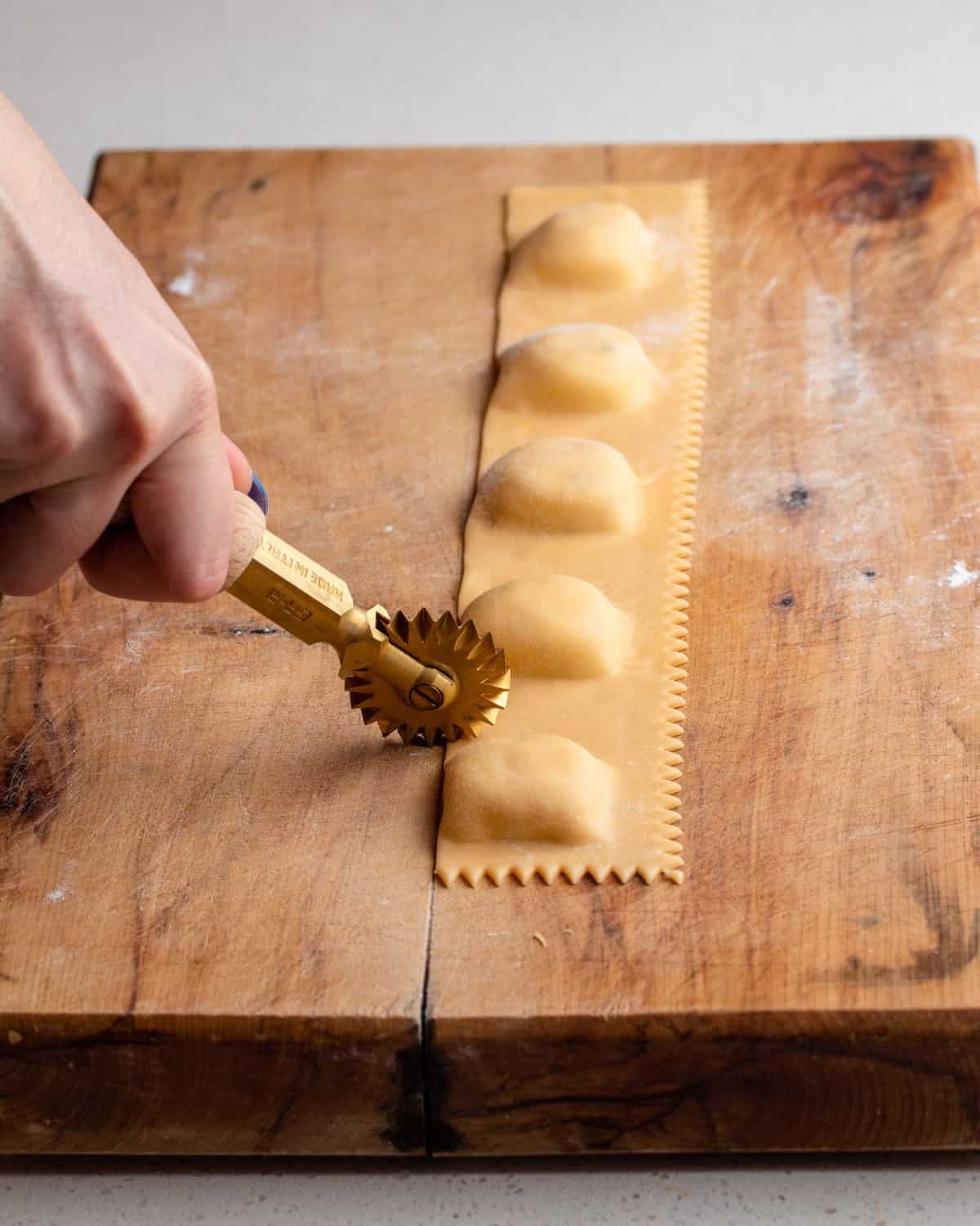 Homemade ravioli being cut on a wooden cutting board.