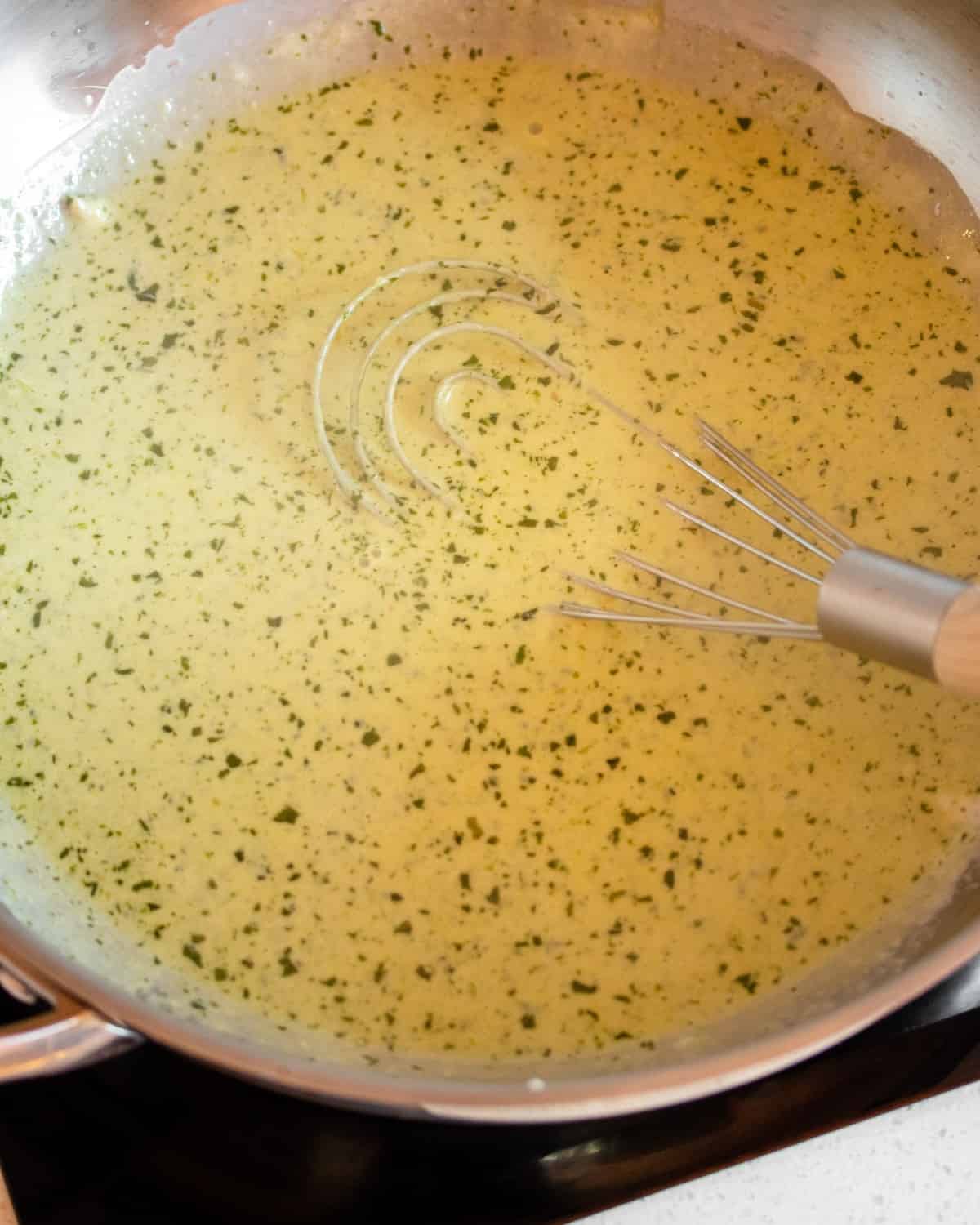 Finished creamy pesto sauce in a pan with a whisk resting.