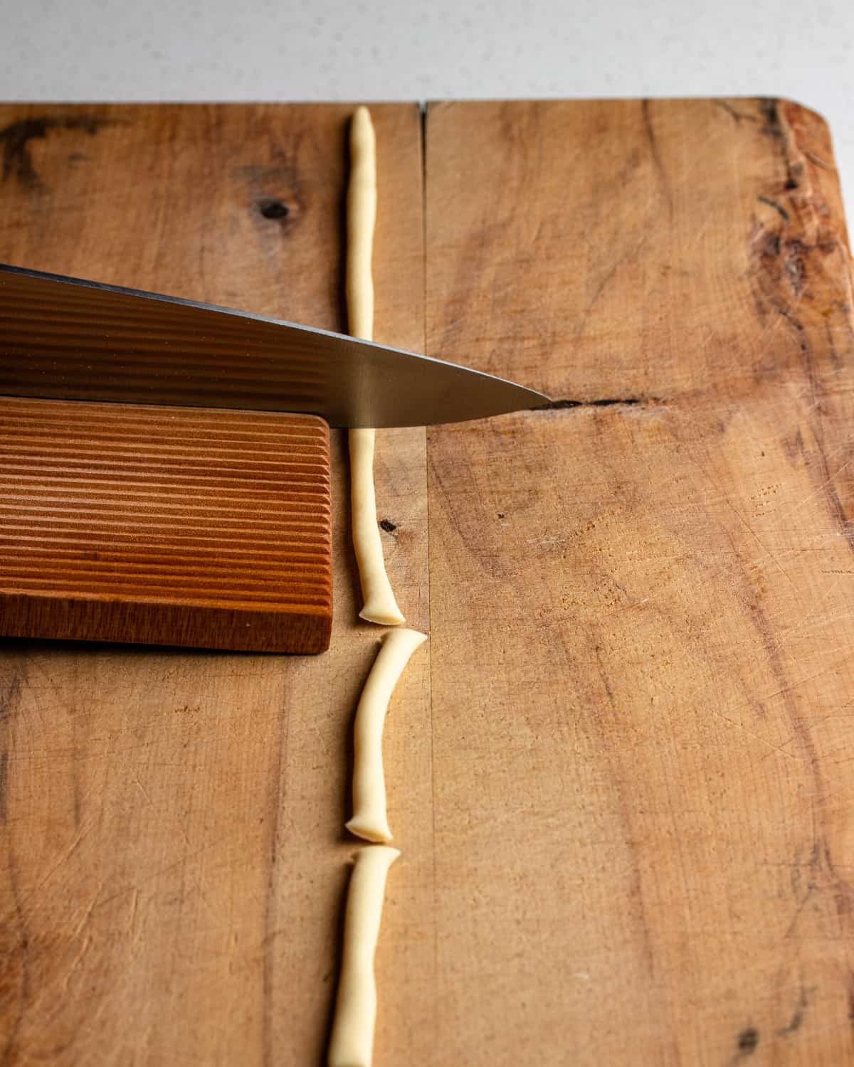 A large knife cutting the pasta strand into narrow lengths.