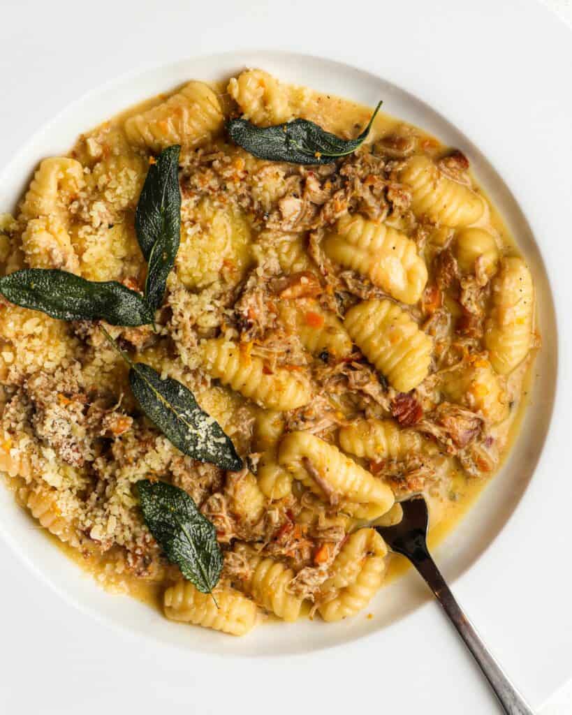 Gnocchi pasta in a white pork ragu sauce. Fork resting in and crisp sage scattered on top.