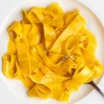 White plate with pappardelle in a golden creamy saffron sauce. Fork resting into pasta.