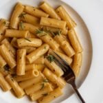 Rigatoni in a glossy garlic butter sauce with a fork piercing into a piece of the pasta. Fresh rosemary on top.