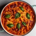 A round casserole dish with baked gnocchi in a tomato sauce. Golden brown cheese top and fresh basil leaves are garnishing.