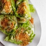Lettuce wedges on a white platter with a creamy dressing and golden panko breadcrumbs on top.