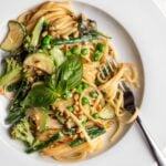 White plate with linguine in a creamy primavera sauce. Zucchini, broccoli and beans are mixed through with peas, pine nuts and lemon zest on top.