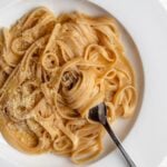 Fettuccine in an alfredo sauce on a white plate. Freshly grated parmesan on top and a fork with noodles twirled around.