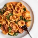 White plate with orecchiette pasta in a creamy sauce with sun dried tomatoes.