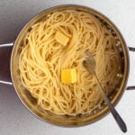 Drained spaghetti in a colander with two knobs of butter on top.