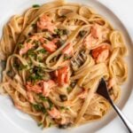 White plate with fettuccine pasta in a creamy salmon sauce. Chunks of salmon and fresh chopped chives on top.