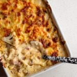 Cauliflower cheese in a rectangle white baking dish. Golden brown top and a spoon digging in.