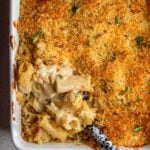 Baked cauliflower mac and cheese in a white porcelain dish. Spoon digging in and a golden brown topping.