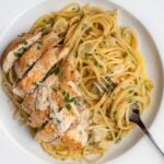 White plate wth spaghetti and sliced gldne brown chicken on top. Fork resting with noodles twirled around it.