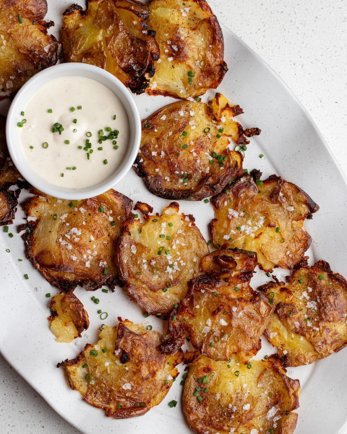 Crispy smashed potatoes on a platter with a ramekin of aioli.