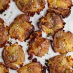 Crispy smashed potatoes on baking paper. Sprinkled with flakey salt and chives.