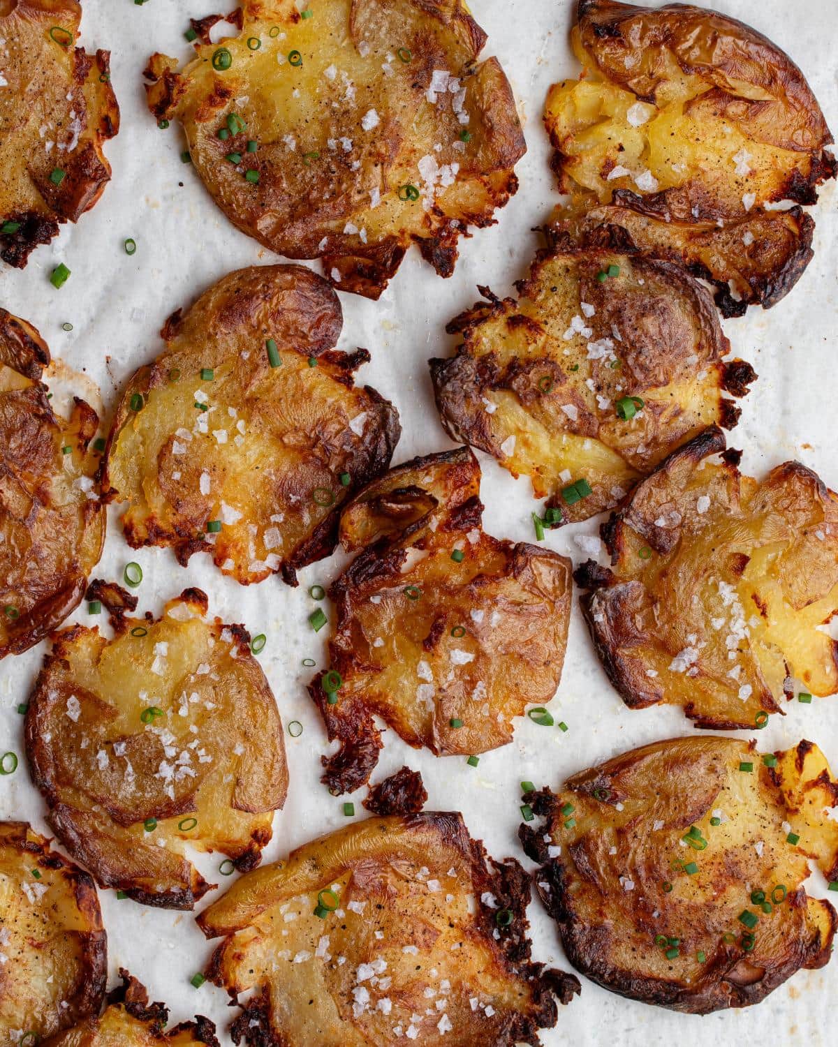 Crispy smashed potatoes on baking paper. Sprinkled with flakey salt and chives.