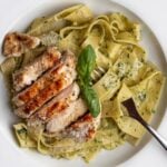 White plate with pappardelle in a creamy pesto sauce. Sliced chicken breast on top.