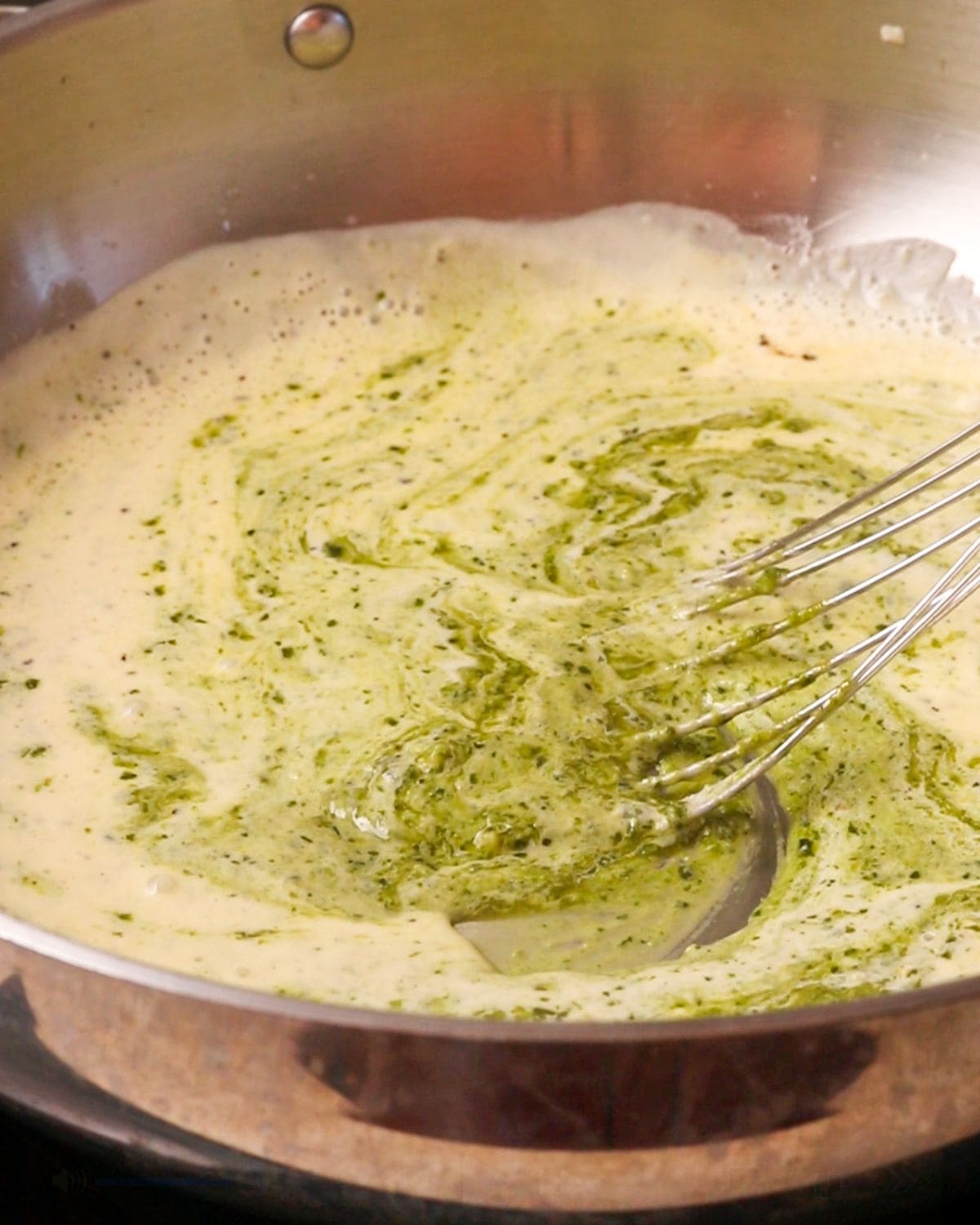 Green basil pesto being mixed into the cream sauce.