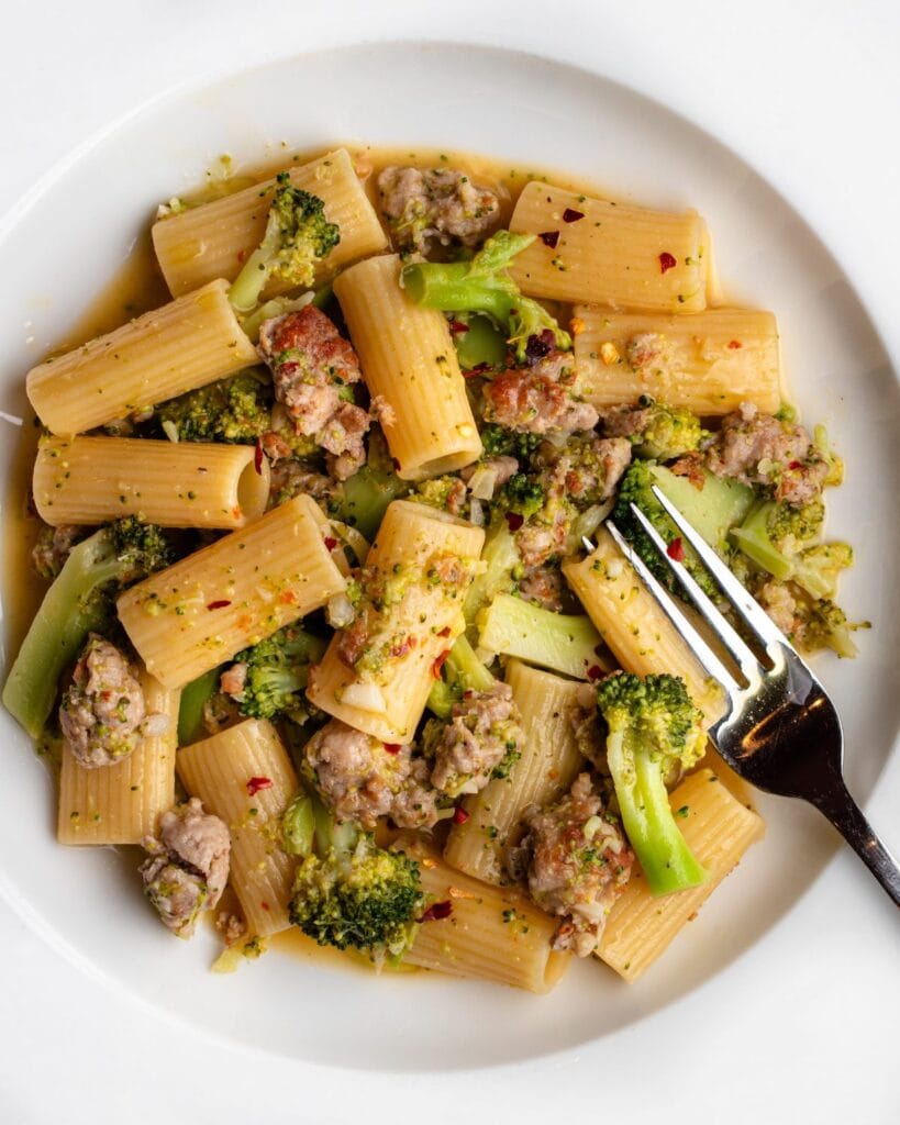 White plate with rigatoni pasta in a sausage and broccoli sauce. Fork resting in to pasta.