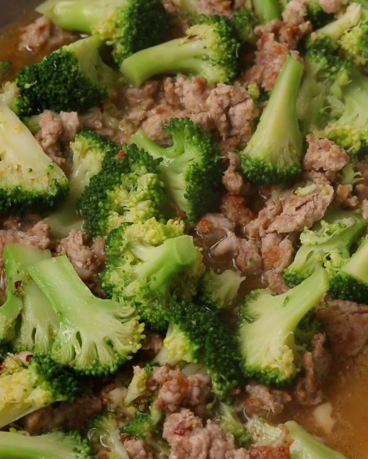 Broccoli and sausage simmering in a pan.