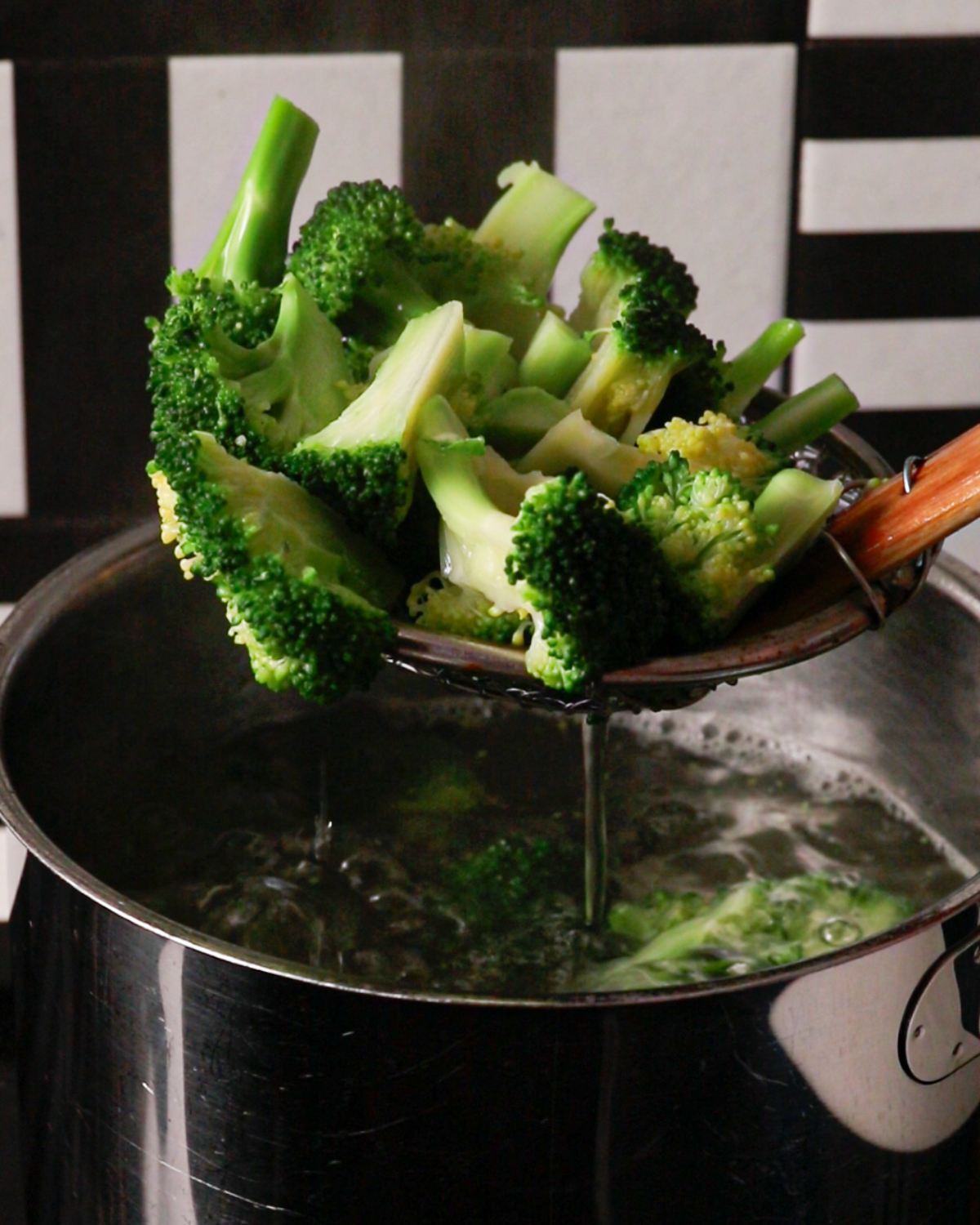 Boiled broccoli being lifted out of a sauce pan with a spider strainer.