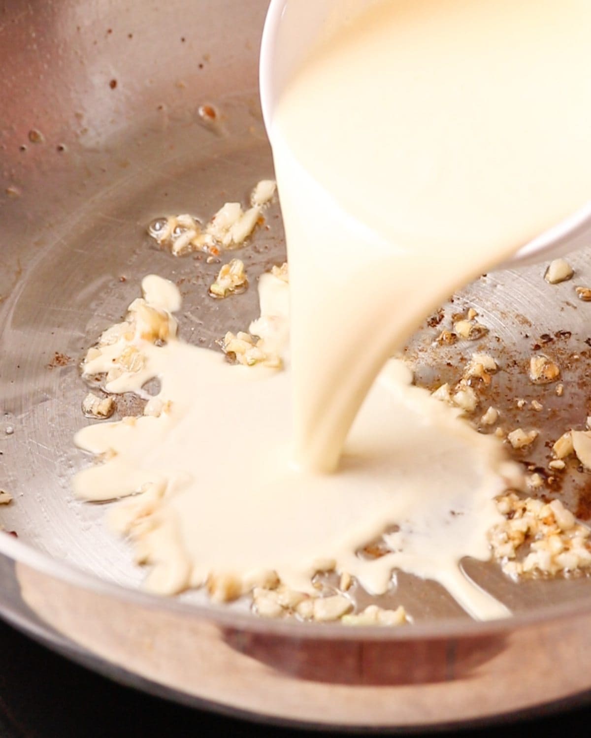 Cream being poured into a pan with chopped garlic.