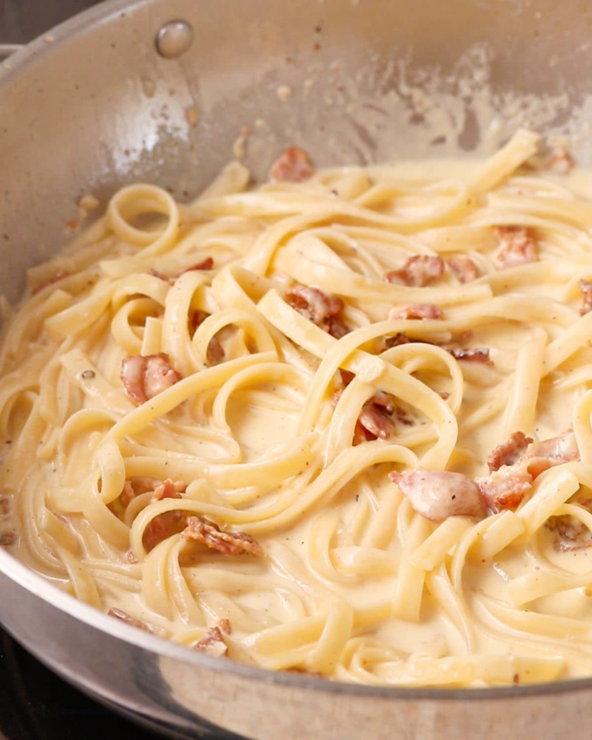 Cooked fettuccine mixed into the sauce in the pan.