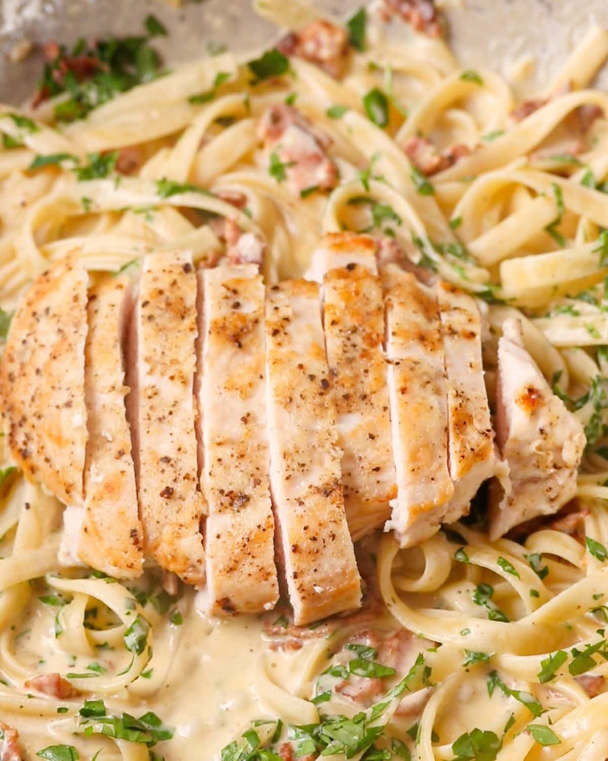 Sliced chicken breast sitting on top of pasta in the pan.