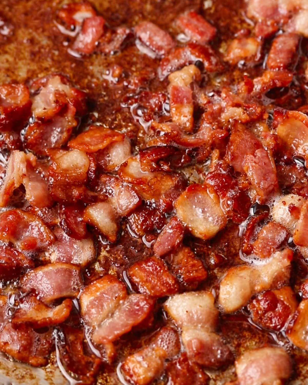 Chopped golden brown bacon pieces sizzling in a pan.